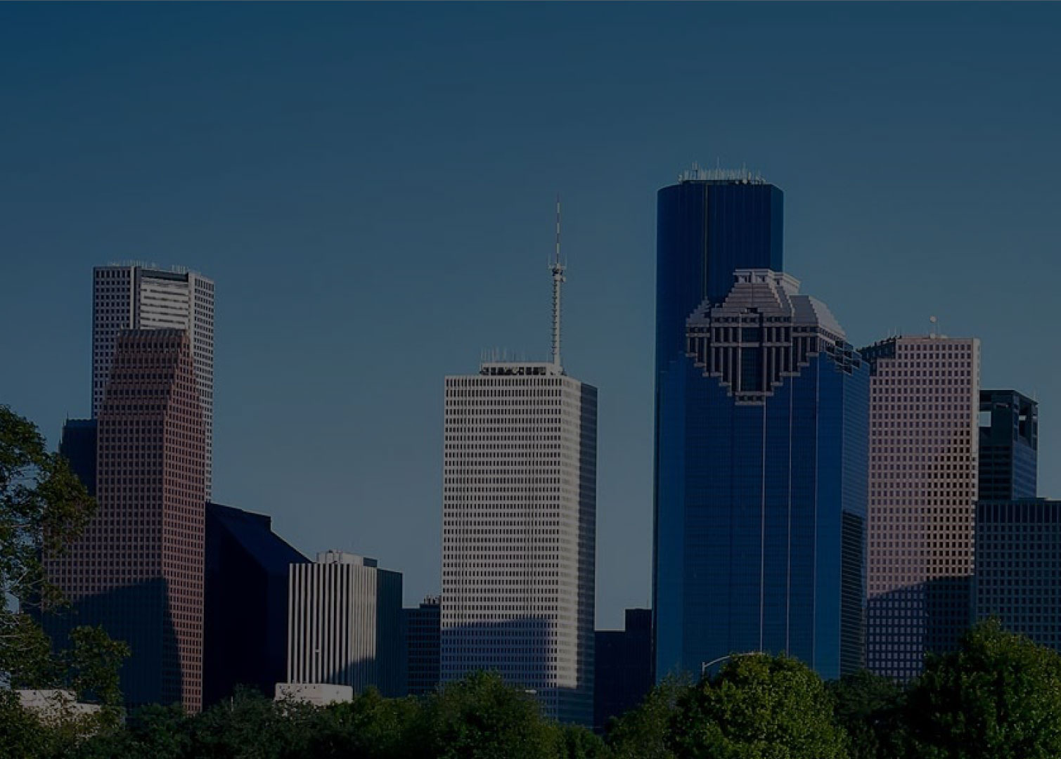 Downtown city skyline with tall modern skyscrapers and office buildings, seen from a distance with green trees in the foreground—a vibrant hub where estate planning professionals shape the future beneath a clear blue sky.