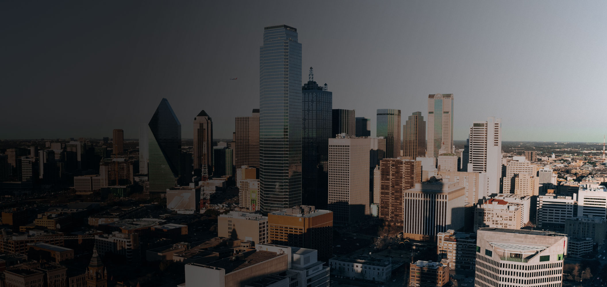 A city skyline with tall modern skyscrapers under a clear sky, some buildings in shadow and others brightly lit by the sun—much like the contrast seen in the work of a dedicated criminal defense attorney.