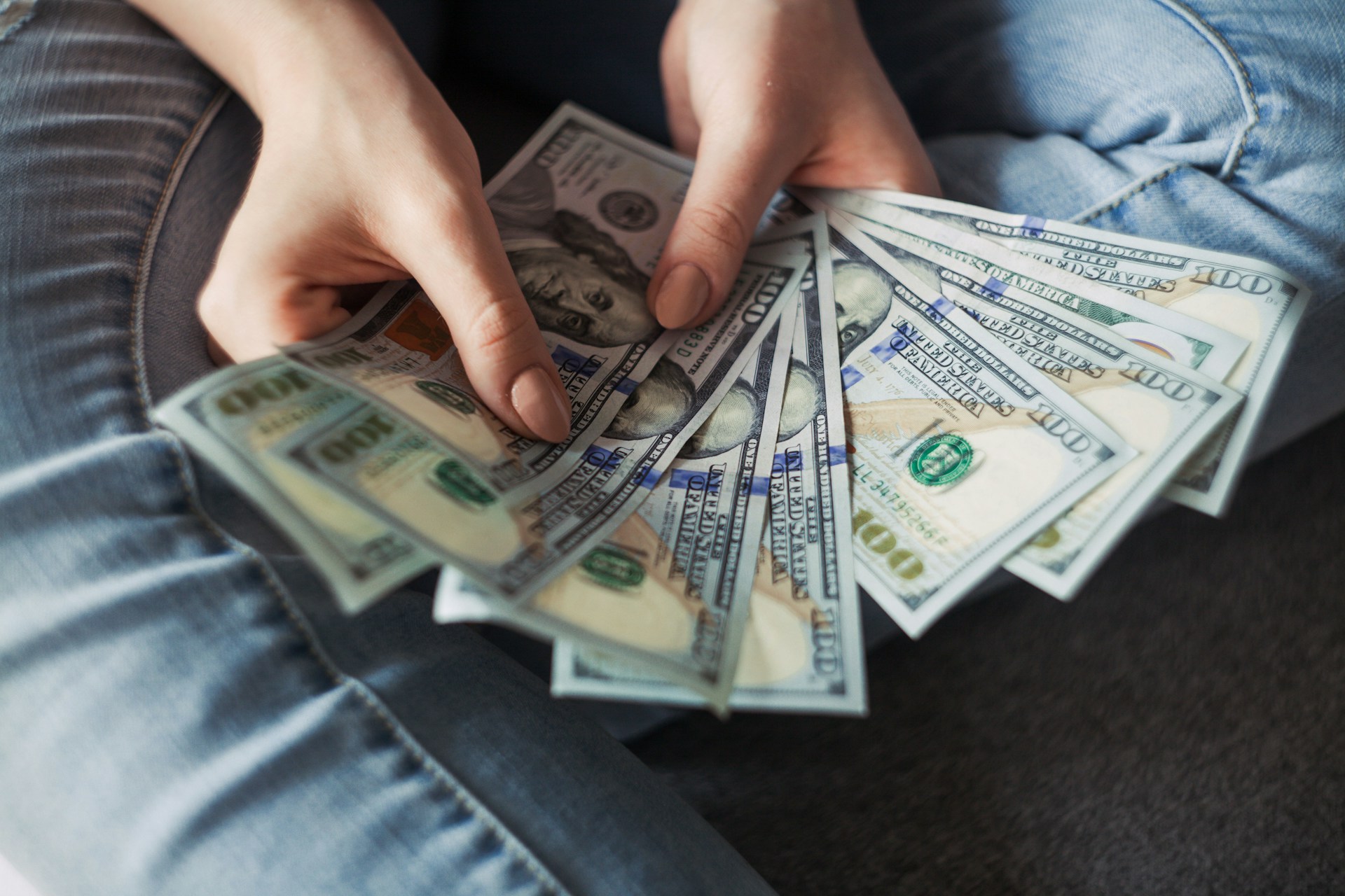 A person wearing jeans is sitting and holding several 0 bills, fanning them out in their hands—perhaps a subtle nod to the proceeds of white-collar crimes.