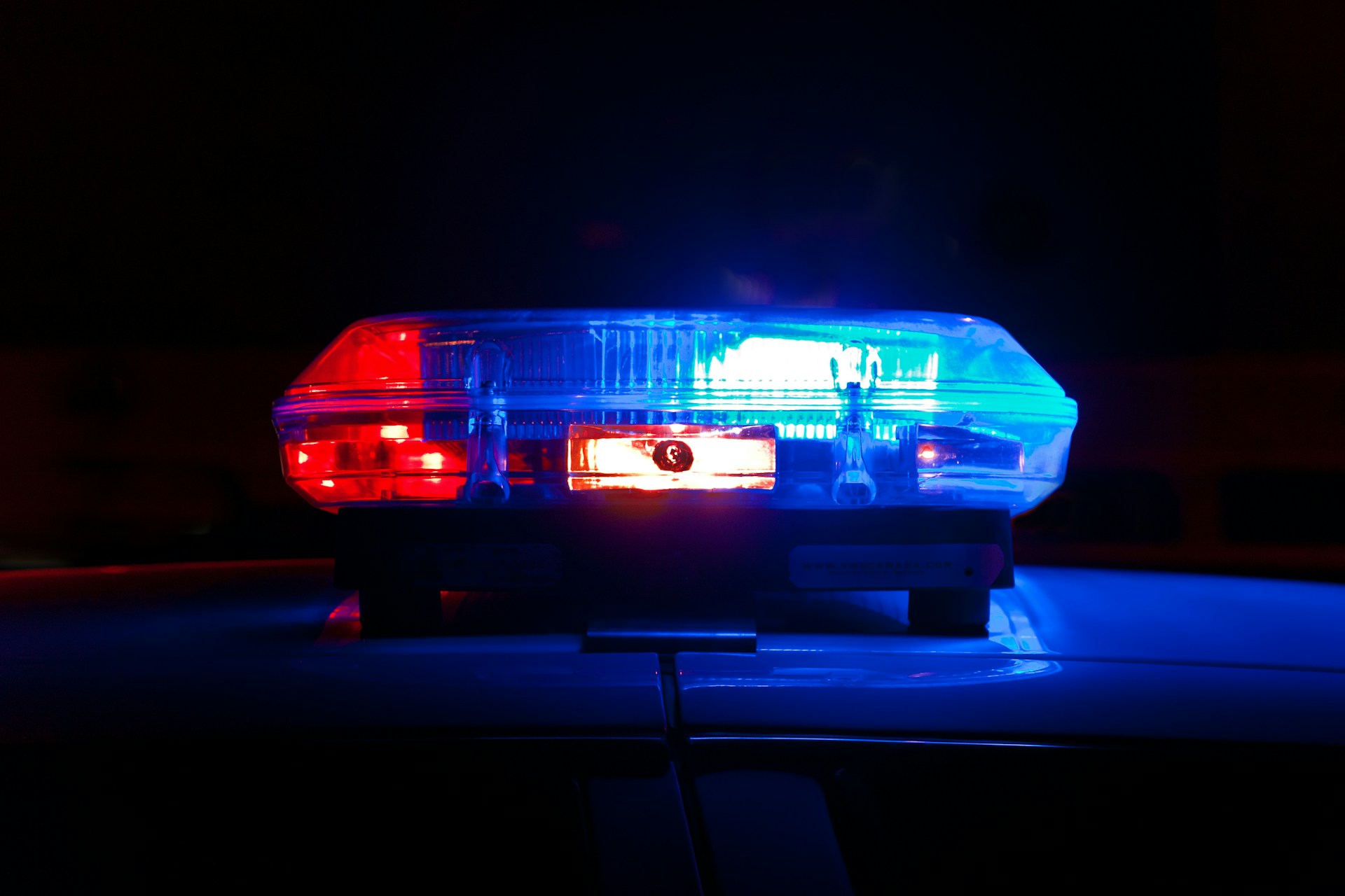 A close-up of a police car's roof with red and blue emergency lights flashing in the dark, responding to a report of someone fleeing an accident.