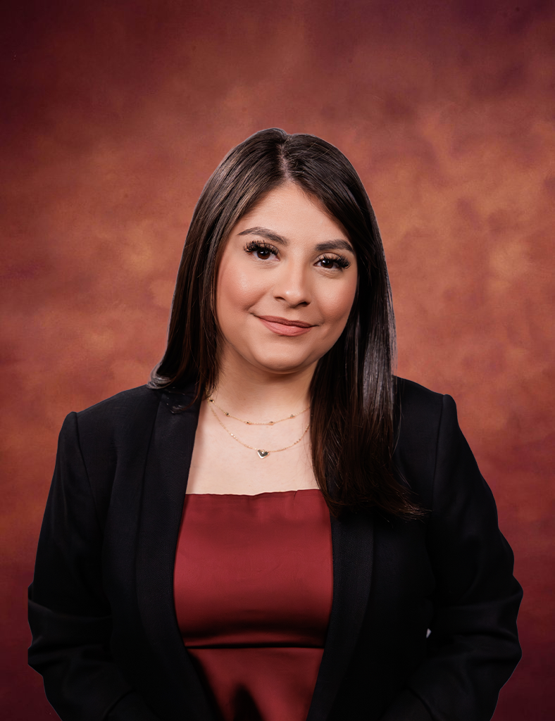 Lizbeth Rebuelta, with straight dark hair, smiles slightly as she poses in a black blazer over a burgundy top against a warm, reddish-brown studio background.