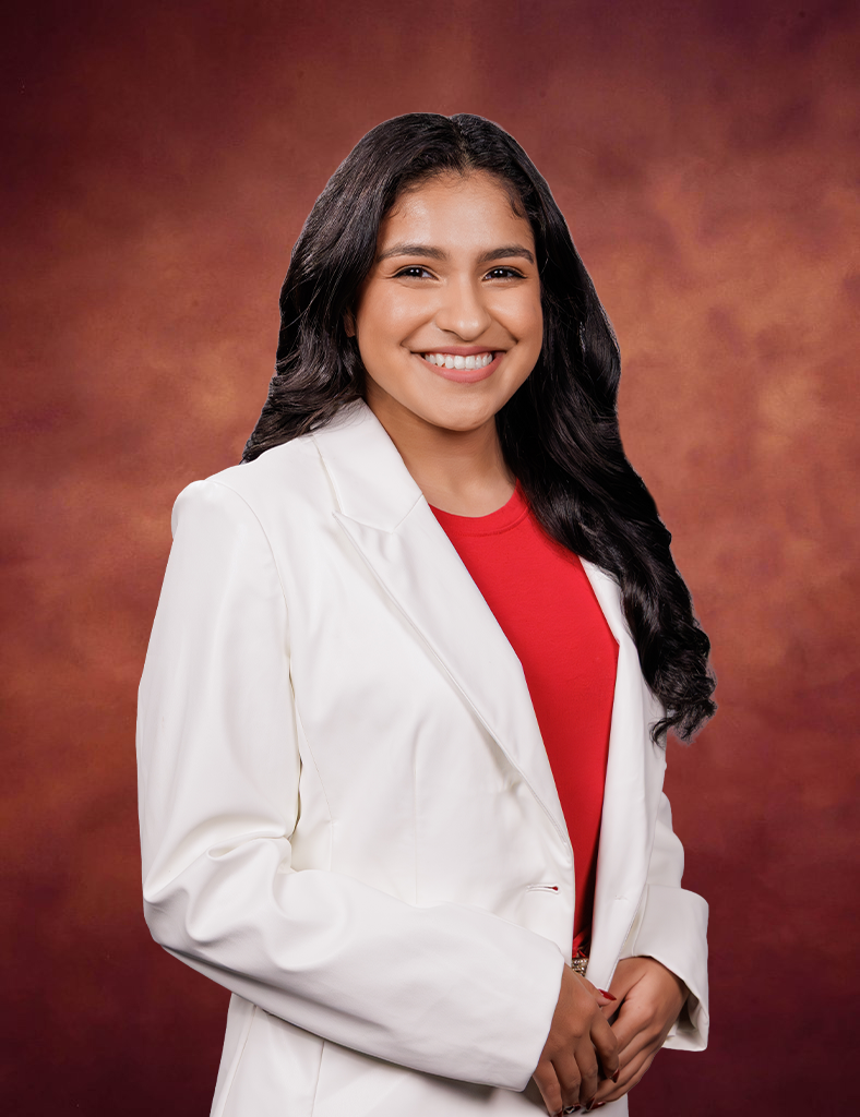 Isabella Lara, with long dark hair, stands smiling in a white blazer over a red top against a warm brown gradient background.