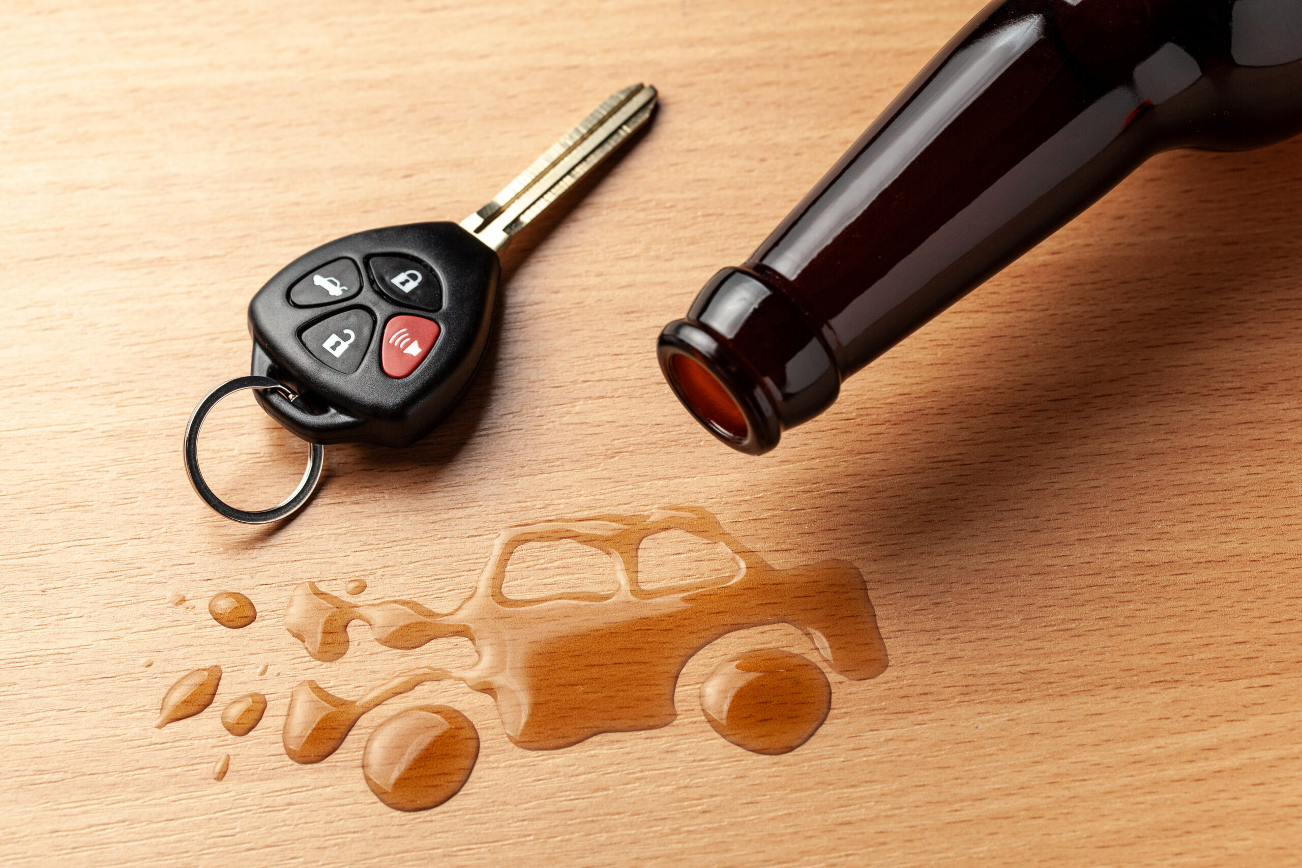 A car key and an overturned beer bottle on a wooden surface, with spilled liquid forming a car shape—powerfully symbolizing the dangers of drinking and driving and the consequences that may lead to a field sobriety test.